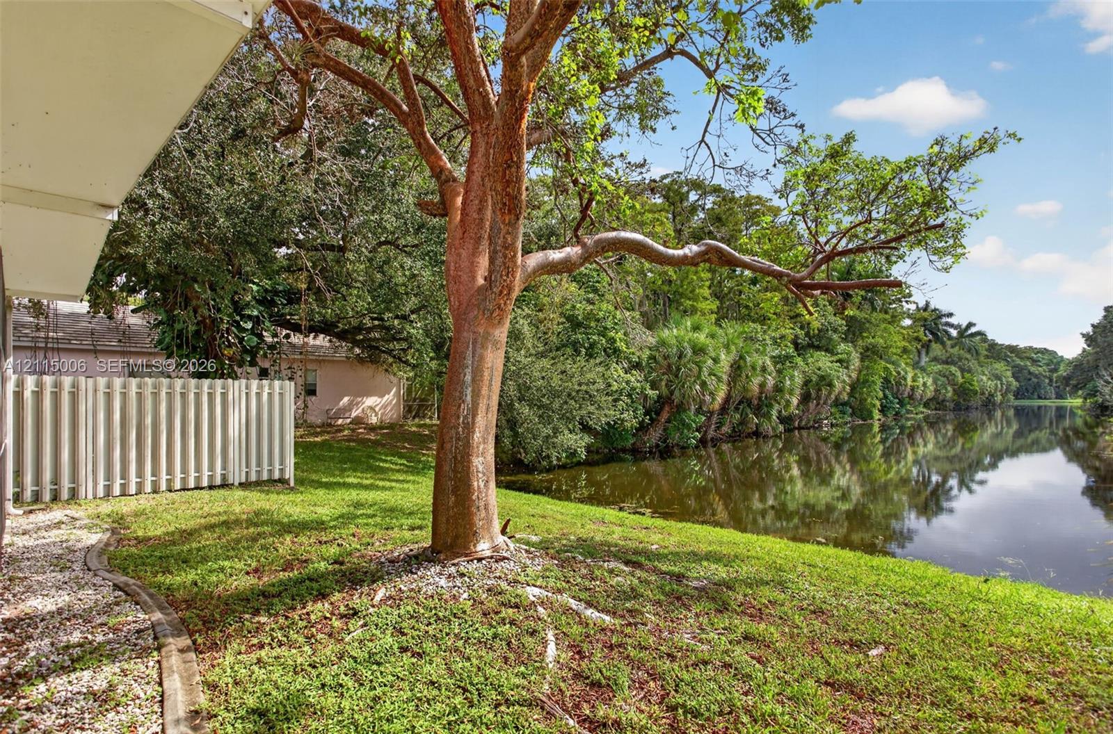 Waterfront backyard featuring a grass lawn, mature trees, and a privacy fence