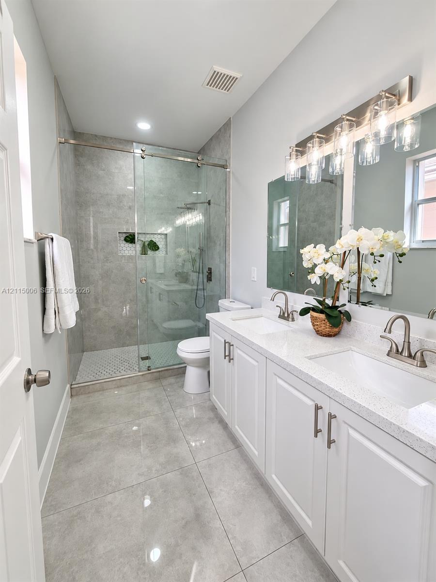 Double vanity featuring white shaker-style cabinetry, quartz countertops, and dual undermount sinks, complemented by a walk-in shower with a glass enclosure, floor-to-ceiling tile surround, and polished nickel fixtures