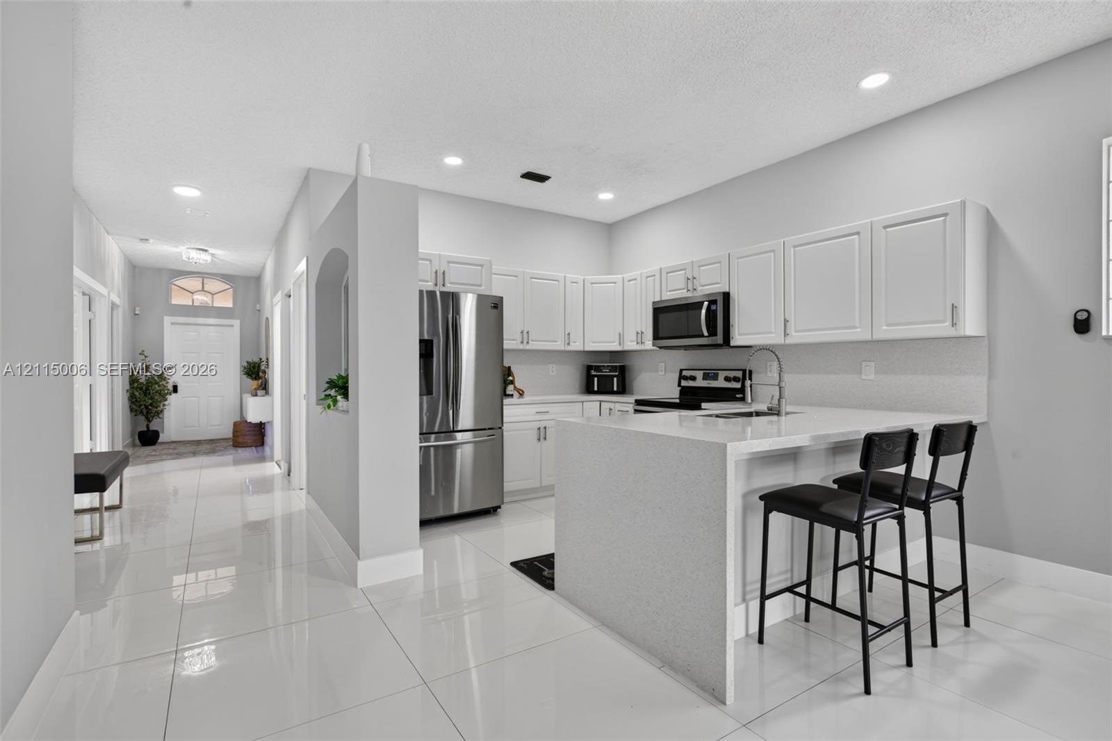 Kitchen featuring white cabinetry, solid surface countertops, stainless steel appliances, a peninsula with seating space, and polished tile flooring Kitchen featuring white cabinetry, solid surface countertops, stainless steel appliances, a peninsula with seating space, and polished tile flooring