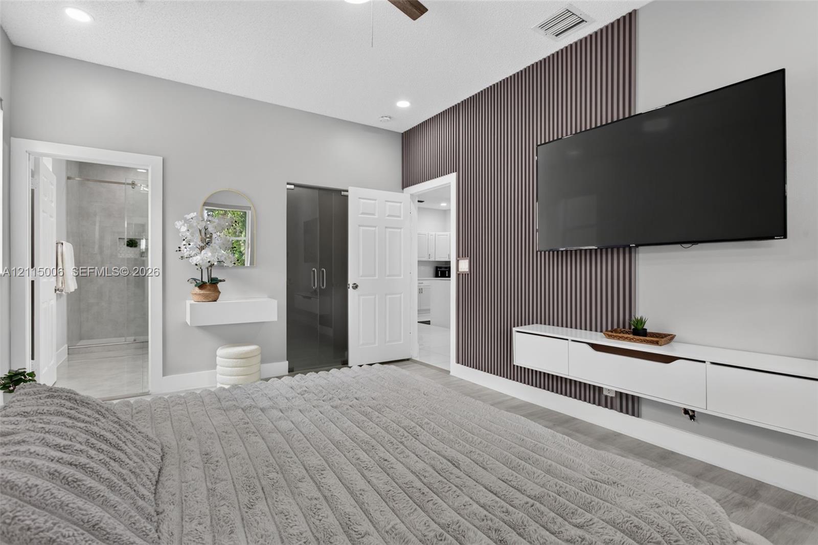 Vertical slat wood-finish accent wall, wall-mounted white media console, recessed ceiling lighting, ceiling fan, and floating wall shelf