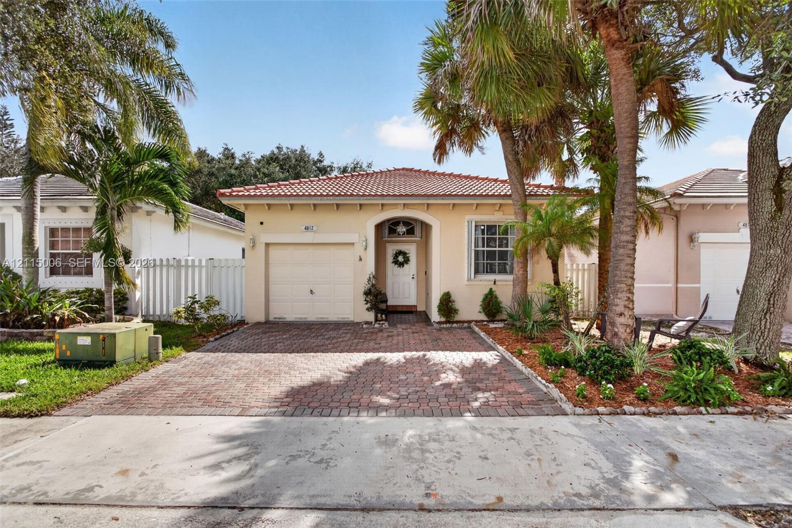 Single-story residence featuring a tile roof, paver driveway, arched entryway, and mature palm trees Single-story residence featuring a tile roof, paver driveway, arched entryway, and mature palm trees