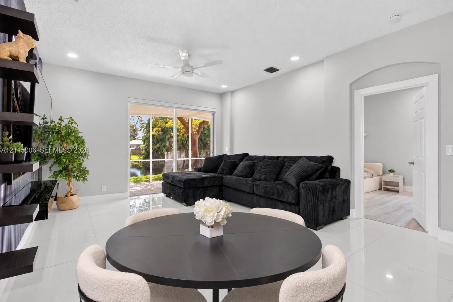 Living area featuring polished tile flooring, recessed lighting, a ceiling fan, wall-mounted display shelving, and sliding glass doors with a screen-enclosed patio Living area featuring polished tile flooring, recessed lighting, a ceiling fan, wall-mounted display shelving, and sliding glass doors with a screen-enclosed patio