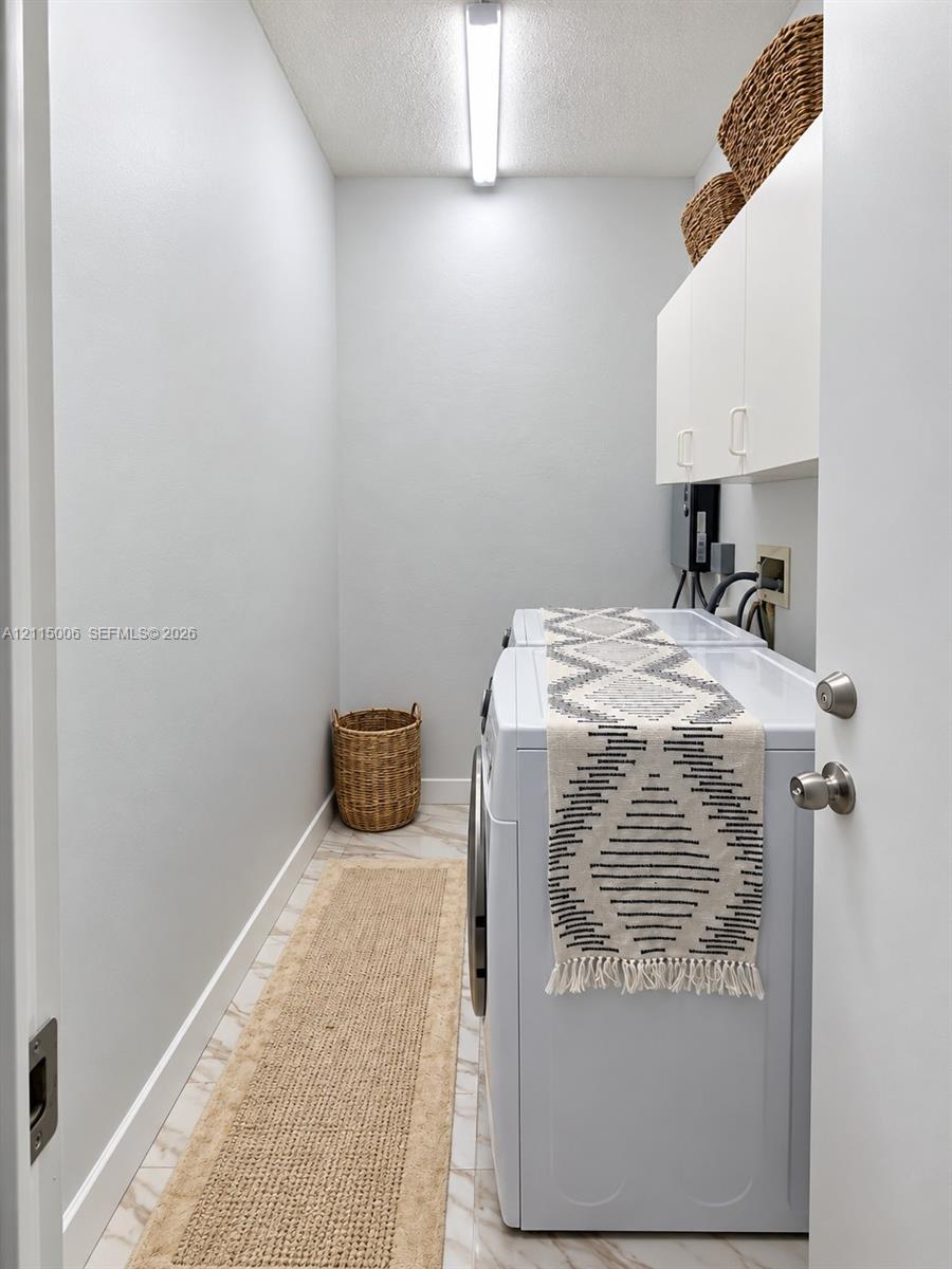 Utility space featuring stone-look tile flooring, white shaker-style wall-mounted cabinetry, and a linear overhead light fixture