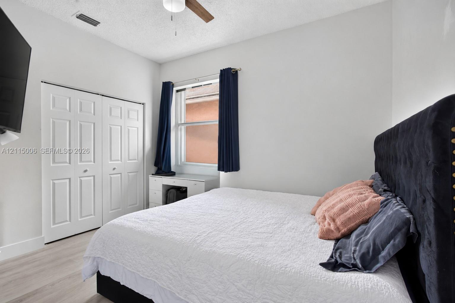 Neutral-toned room featuring wood-finish flooring, a ceiling fan, and double-panel closet doors