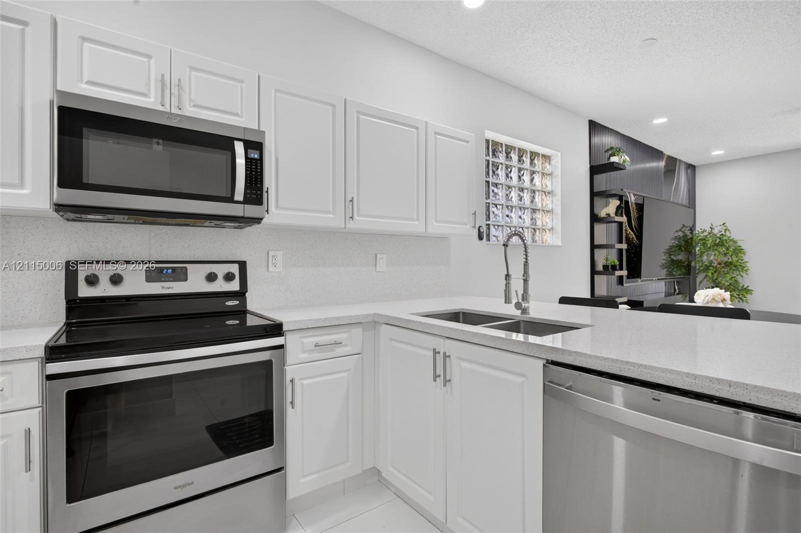 Kitchen featuring white shaker-style cabinetry, stainless steel appliances, light-toned solid surface countertops, a dual-basin stainless steel undermount sink with a gooseneck faucet, and a glass block window
