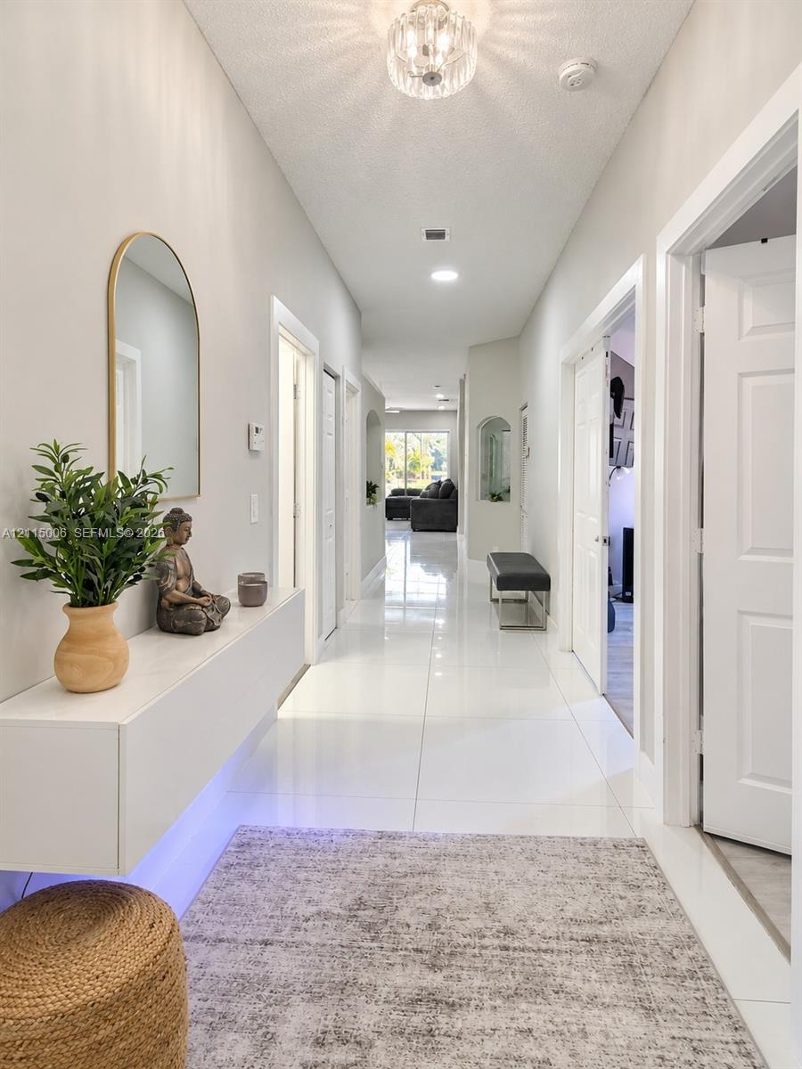 Hallway featuring large-format tile flooring, a wall-mounted floating console, an arched wall mirror, and a decorative flush-mount ceiling fixture Hallway featuring large-format tile flooring, a wall-mounted floating console, an arched wall mirror, and a decorative flush-mount ceiling fixture