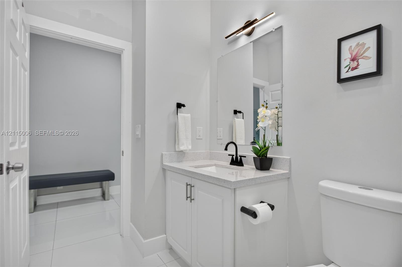 Bathroom featuring a white vanity with a composite stone countertop, rectangular undermount sink, matte black faucet, and linear LED wall-mounted light fixture