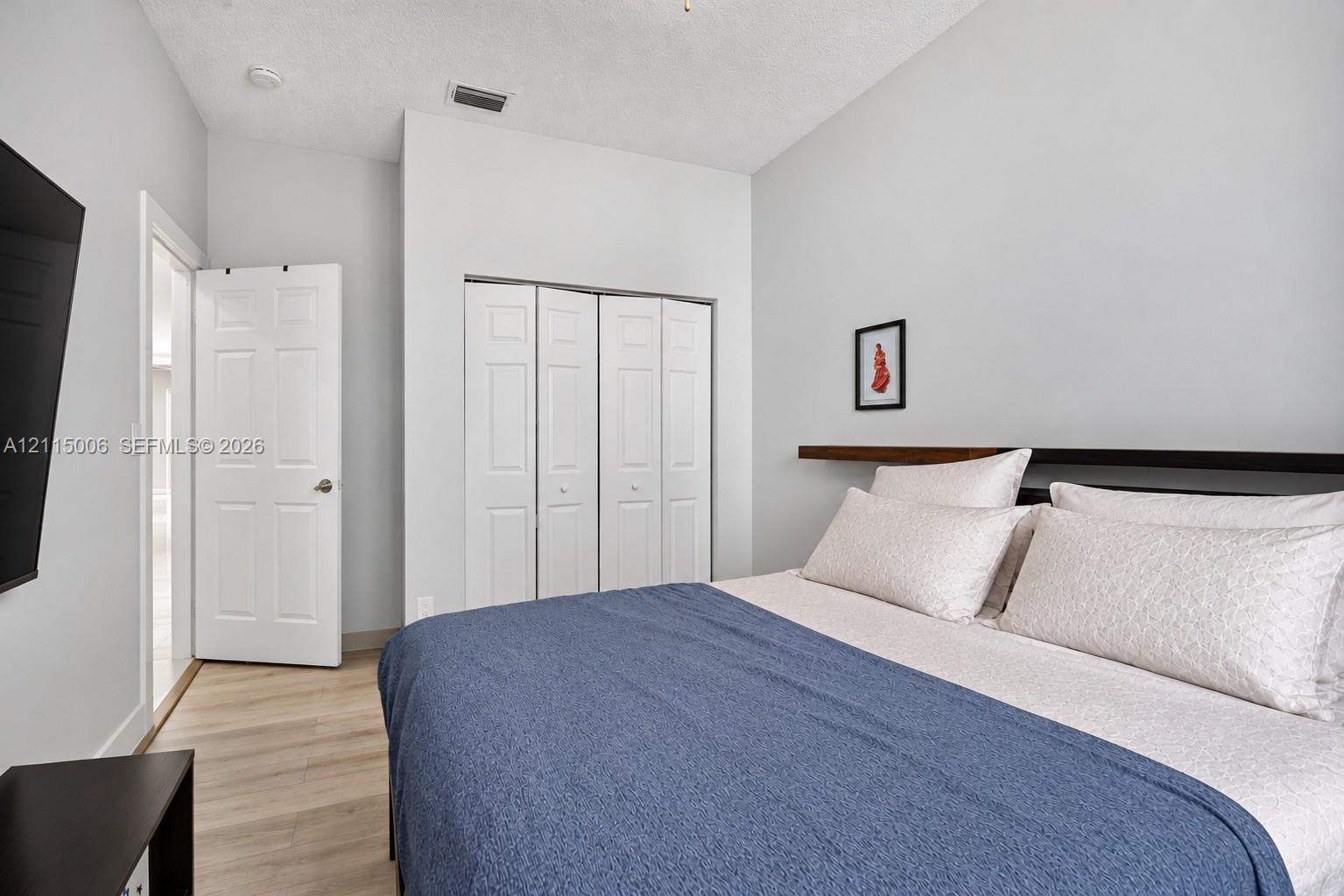 Bedroom featuring wood-finish flooring, a built-in closet with four-panel folding doors, and a wall-mounted wood floating shelf