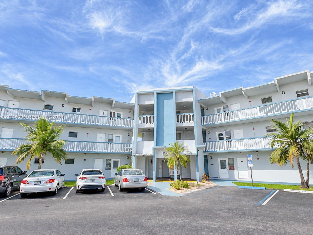 Multi-story exterior featuring light-toned stucco facade, blue accent panels, and covered balconies with white railings