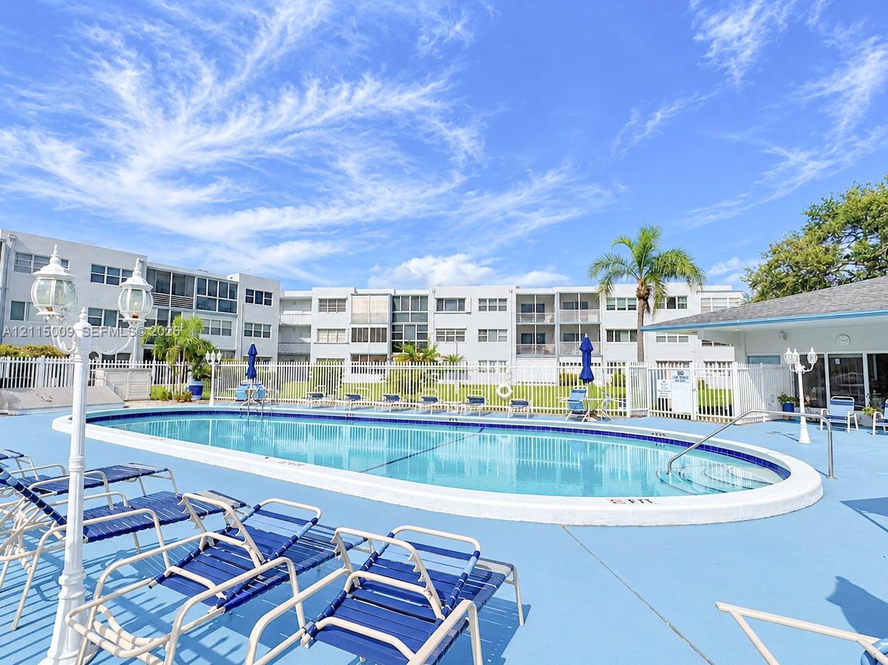 Oval swimming pool with a concrete deck, metal perimeter fencing, and decorative exterior lamp posts
