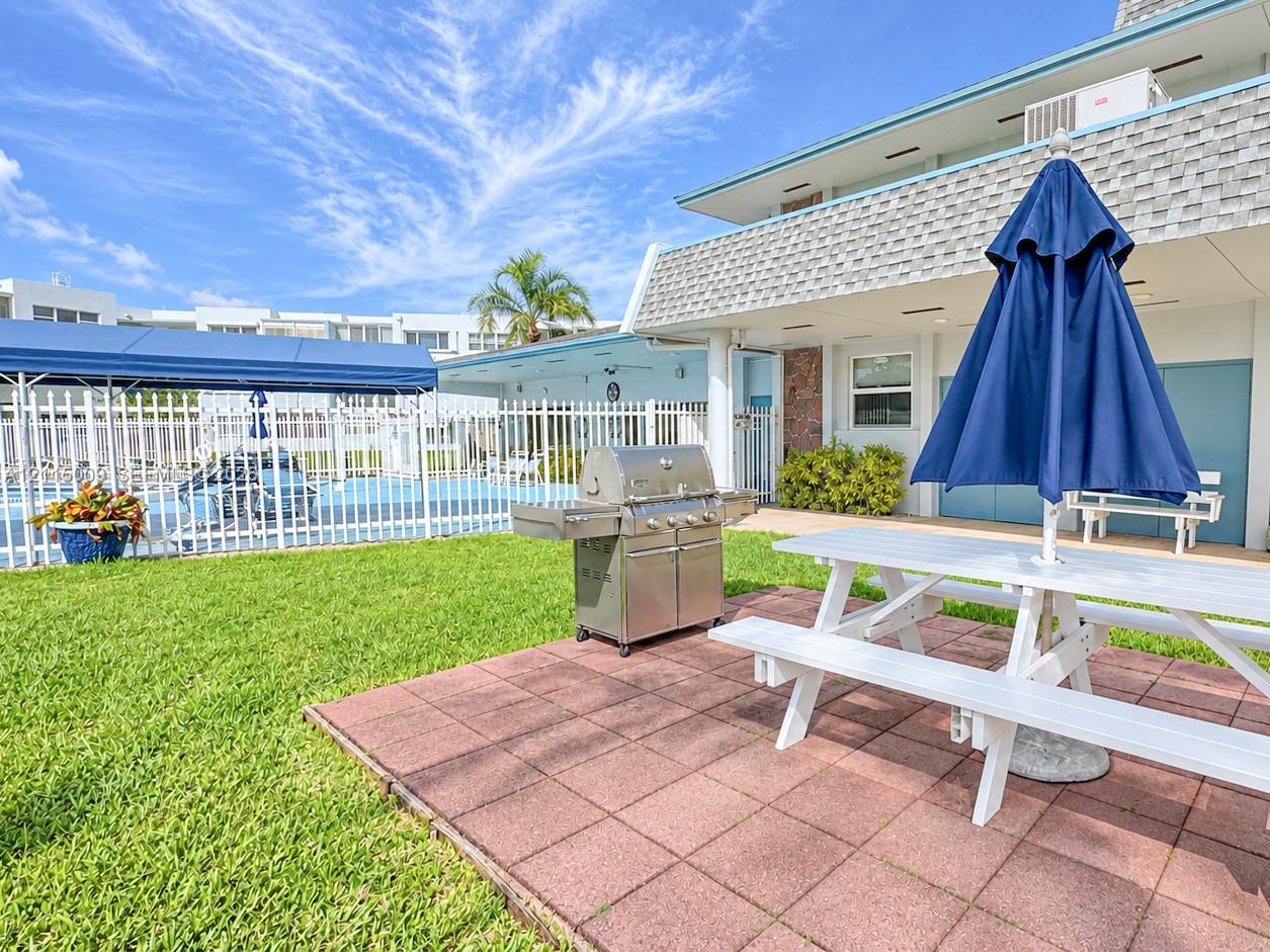 Outdoor space featuring a paved patio, manicured lawn, stainless steel built-in grill, and metal perimeter fencing