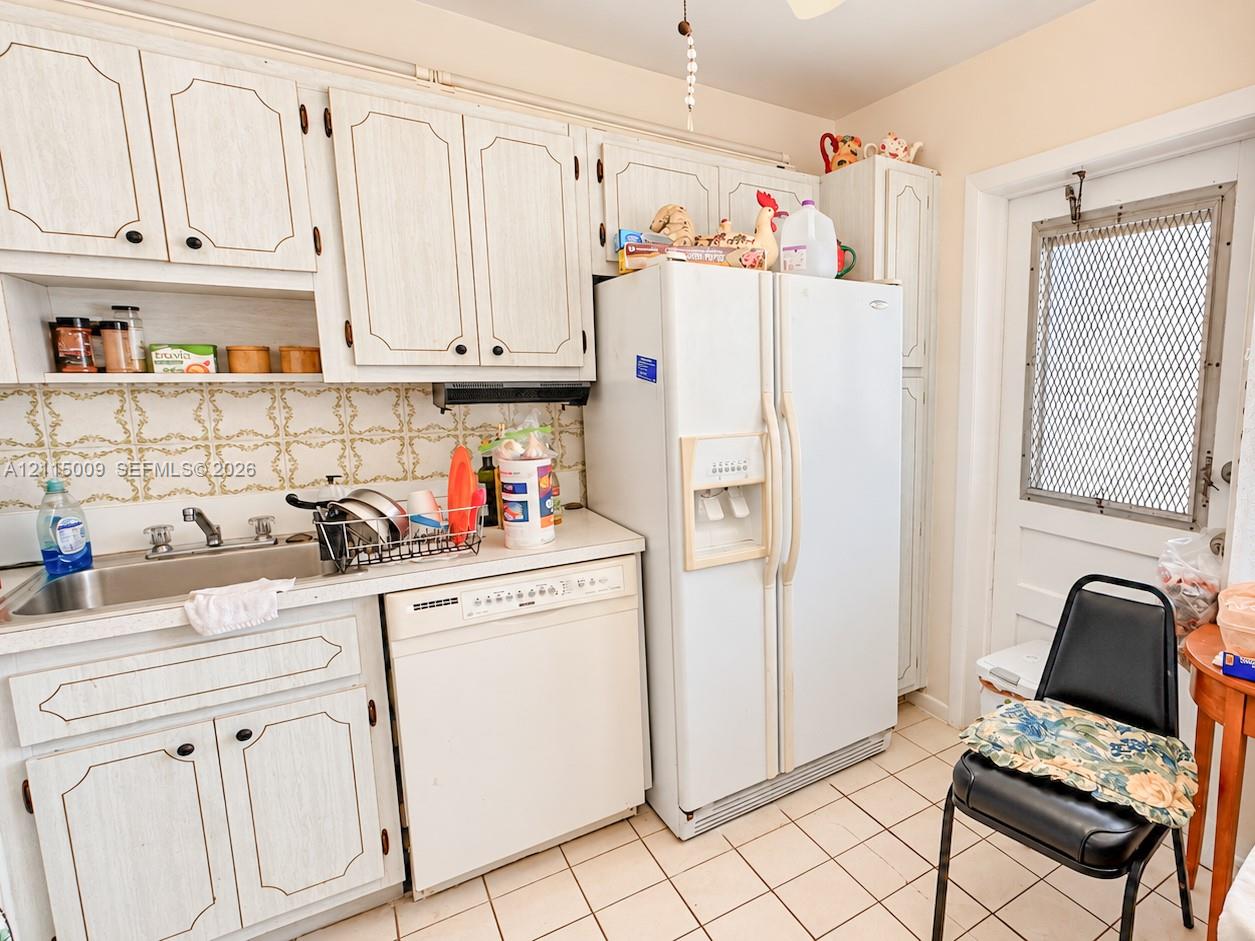 Kitchen featuring white cabinetry, ceramic tile backsplash, integrated stainless steel sink, tile flooring, and a side-by-side refrigerator