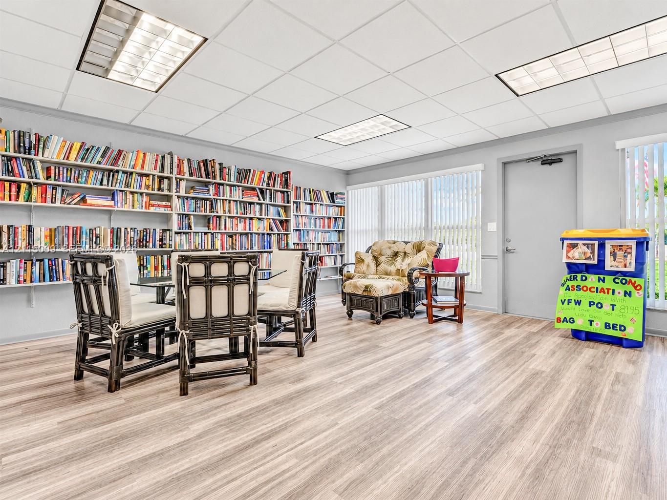 Spacious room featuring floor-to-ceiling built-in shelving, wood-finish flooring, recessed lighting, and expansive windows with vertical blinds