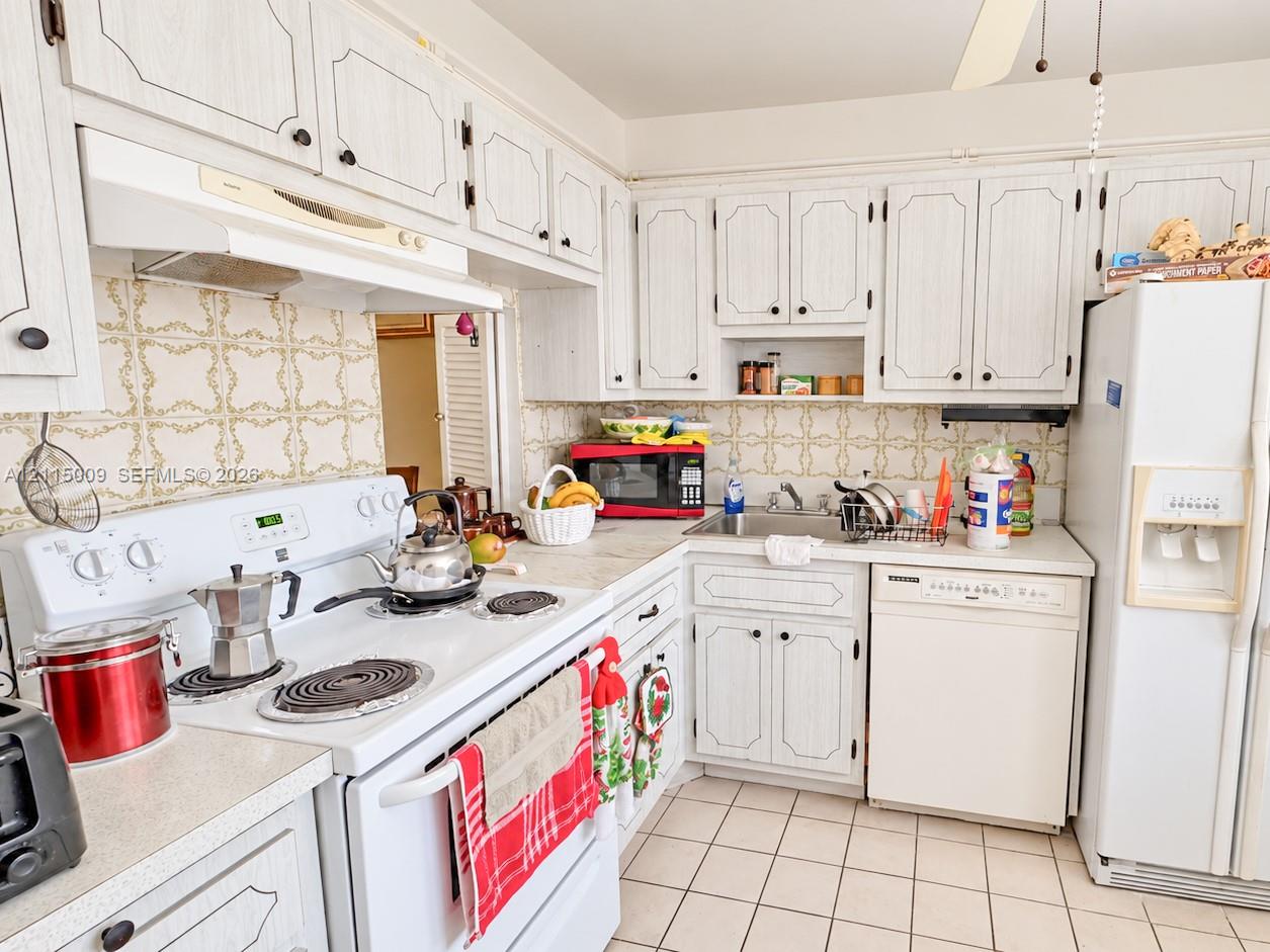 Kitchen featuring white cabinetry with decorative trim, white-finish appliances, light-toned countertops, tile backsplash, and ceramic tile flooring