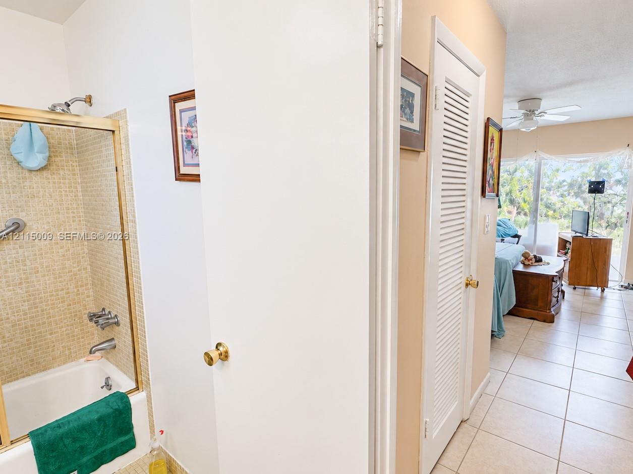 Shower and tub combination with glass-panel sliding door, brass-finish trim, tiled surround, and louvered-panel closet door