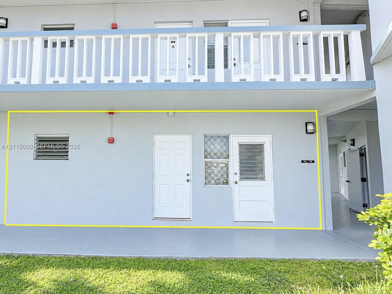 Exterior facade featuring a ground-level concrete patio, a louvered wall vent, solid-core panel doors, and a decorative glass block window accent