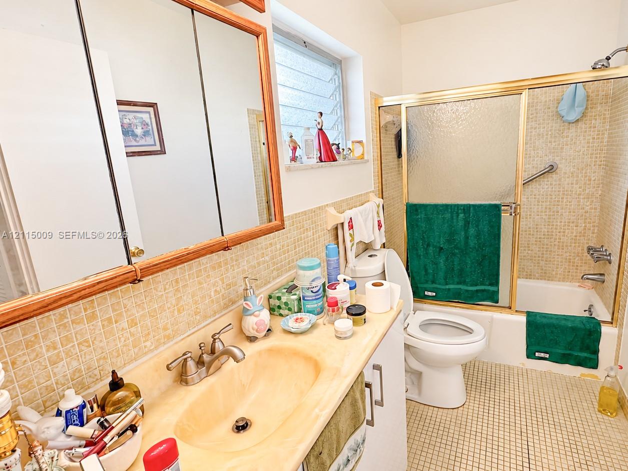 Bathroom featuring a single-basin vanity with an integrated countertop, tri-fold medicine cabinet, louvered window, and a shower-tub combination with sliding glass doors