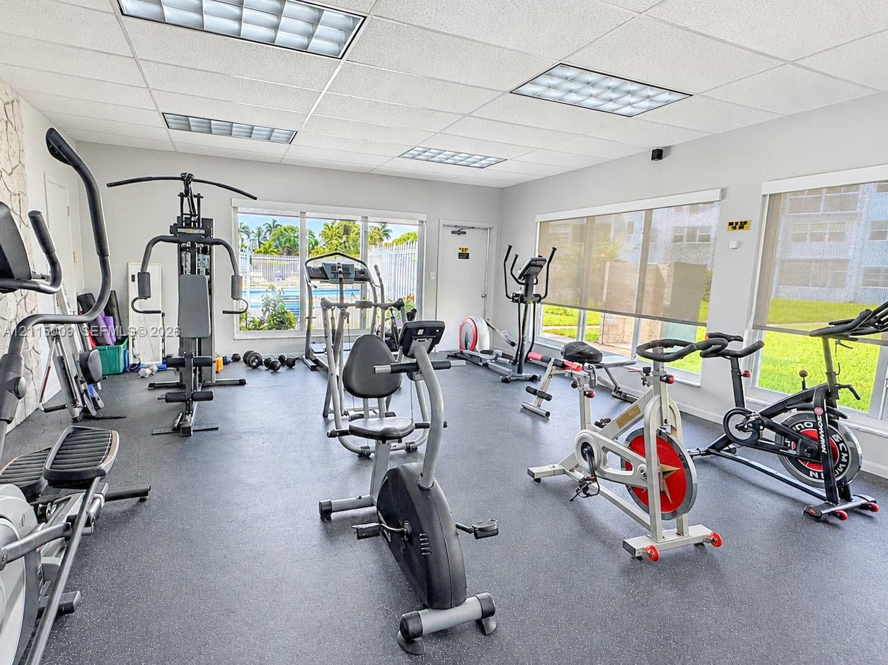 Fitness room featuring rubberized flooring, drop ceiling with recessed panel lighting, and large windows with retractable shades