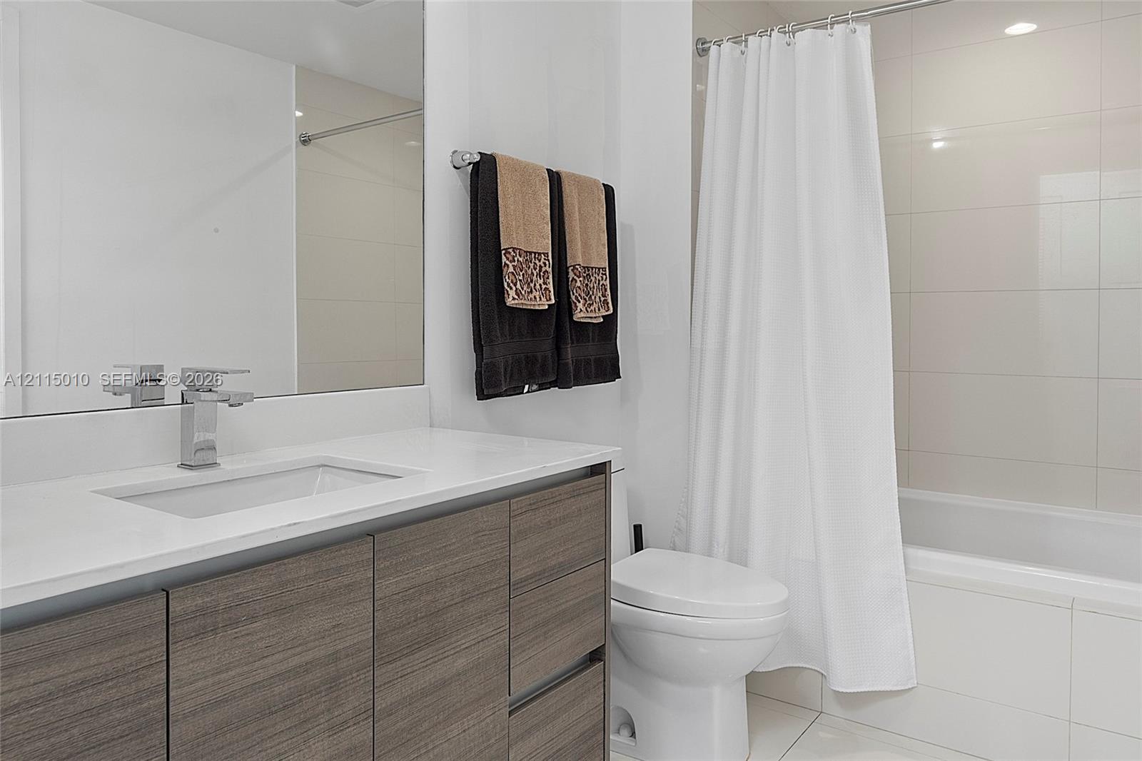 Bathroom featuring a flat-panel wood-finish vanity, rectangular undermount sink, stone-surface countertop, chrome single-handle faucet, and full-height tiled shower surround