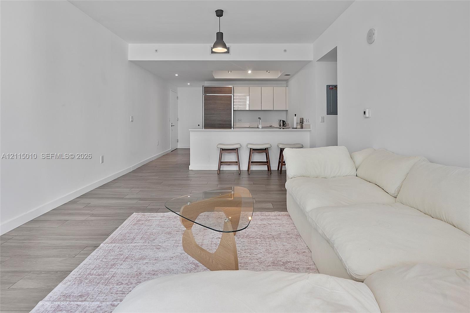 Open-concept interior featuring wood-finish flooring, a kitchen island with stone countertops, modern flat-panel cabinetry, and a minimalist pendant light fixture