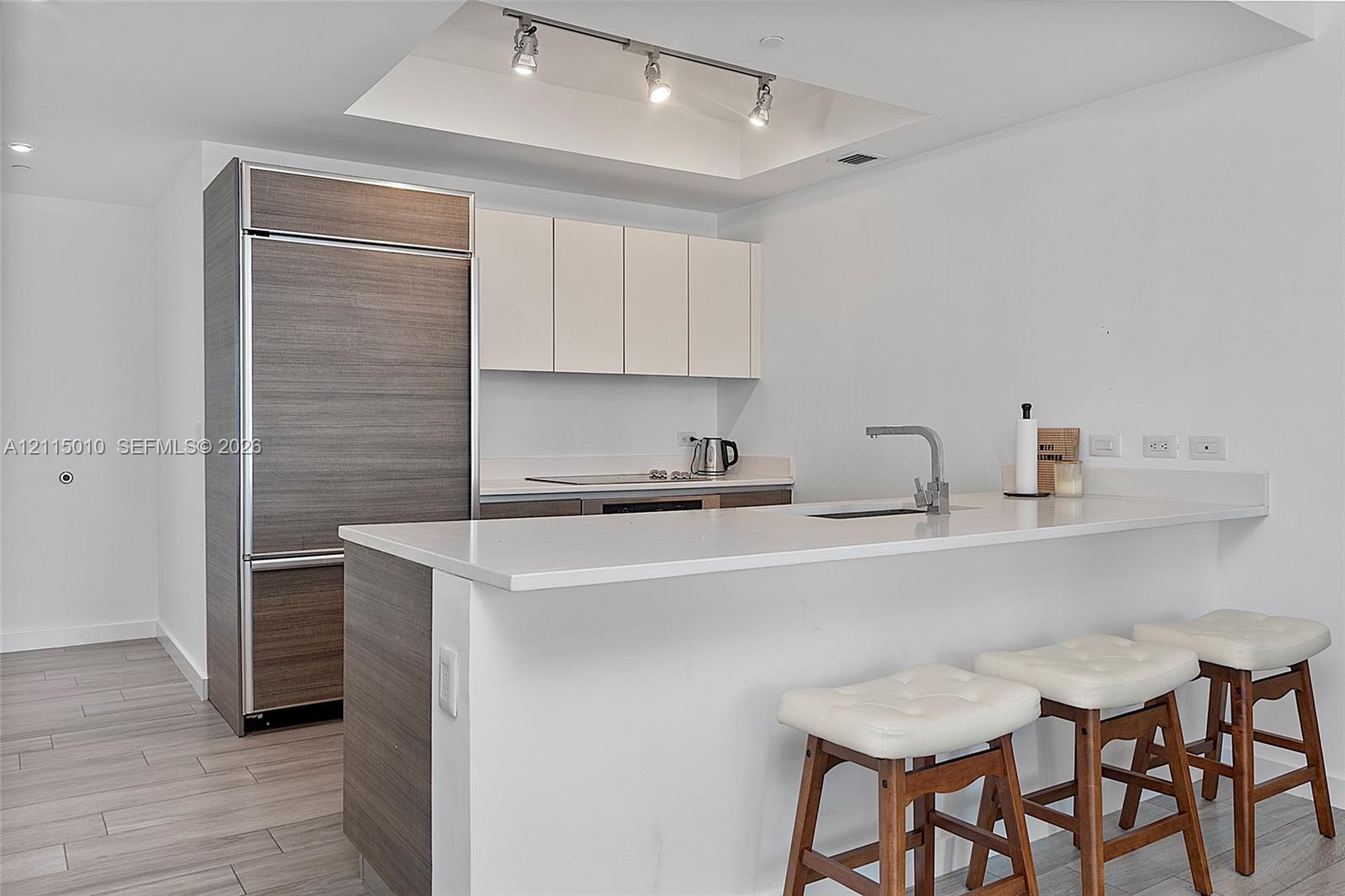 Kitchen featuring a stone-surface island with an integrated sink, custom cabinetry with wood-finish paneling, a paneled refrigerator, recessed ceiling lighting, and wood-finish flooring