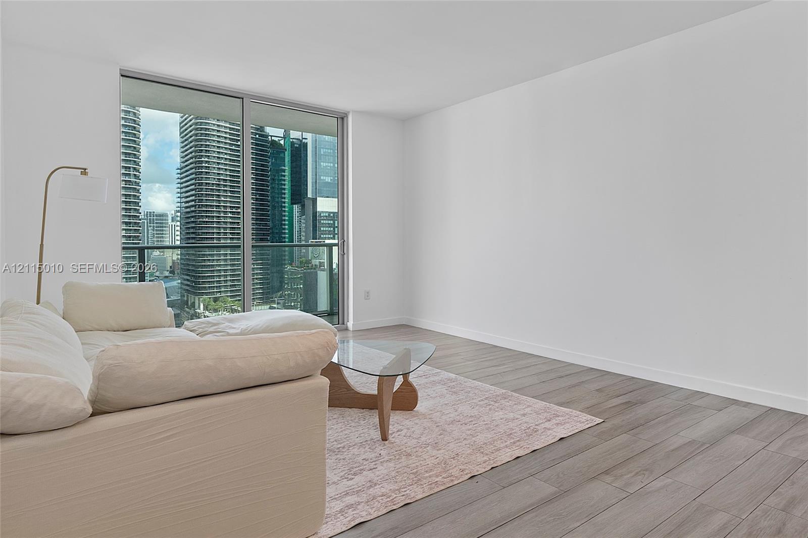 Floor-to-ceiling sliding glass doors, urban skyline backdrop, and wood-finish flooring