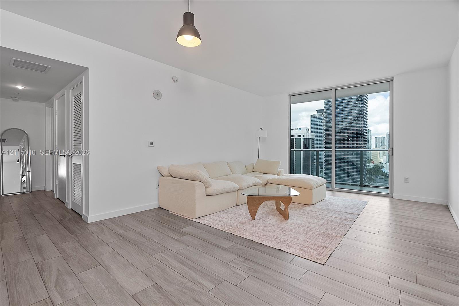 Wood-finish flooring, floor-to-ceiling glass sliding doors, private balcony with metal railing, and pendant lighting Wood-finish flooring, floor-to-ceiling glass sliding doors, private balcony with metal railing, and pendant lighting
