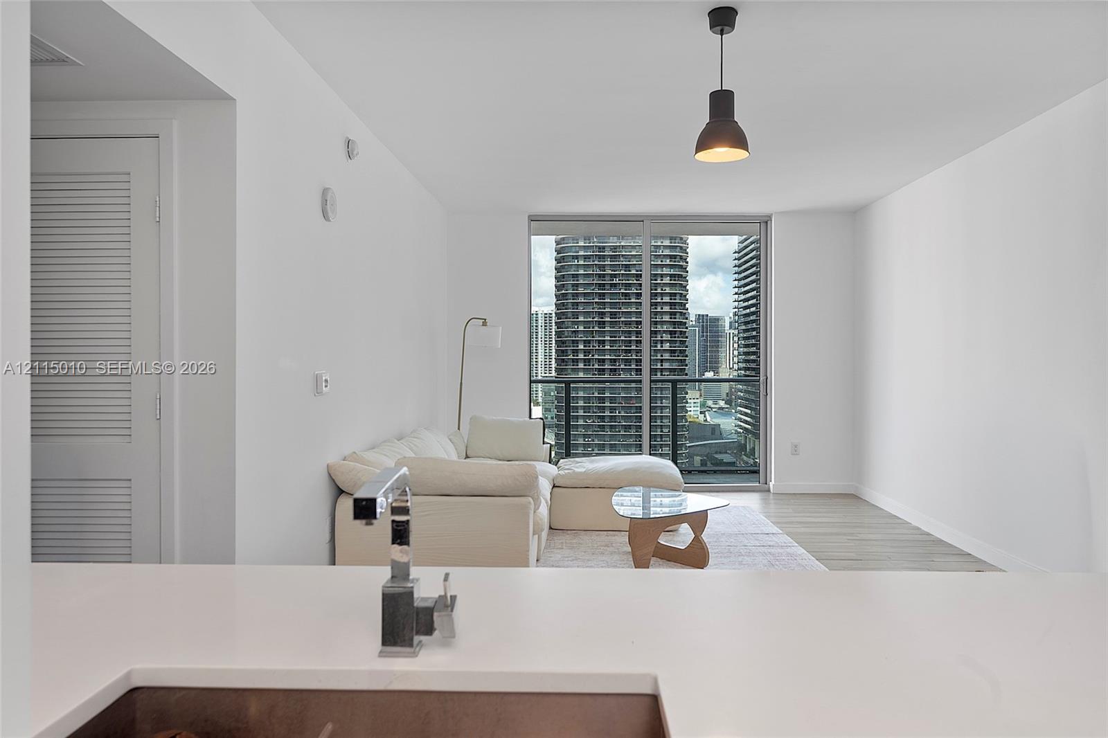 Solid surface countertop with a single-handle chrome faucet, floor-to-ceiling glass sliding doors, wood-finish flooring, and a single black industrial-style pendant light