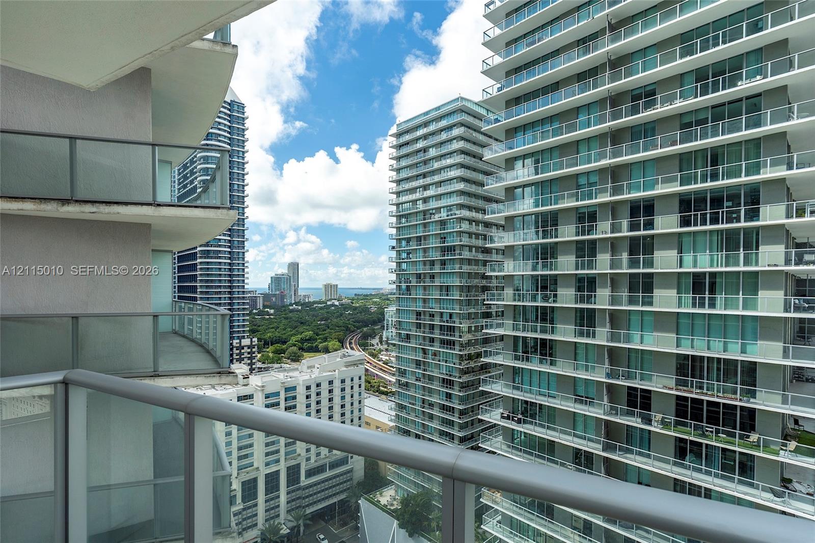 Private balcony featuring a glass-panel railing and metal handrail with an expansive urban skyline outlook