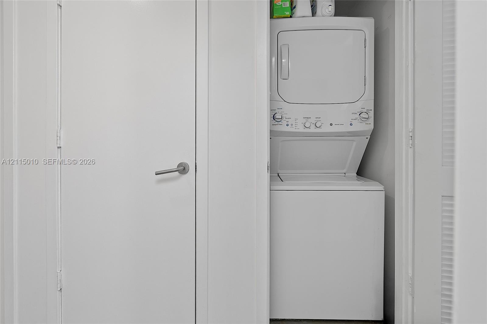 Stacked white laundry unit enclosed in a dedicated closet space with a solid-core door and metal lever handle