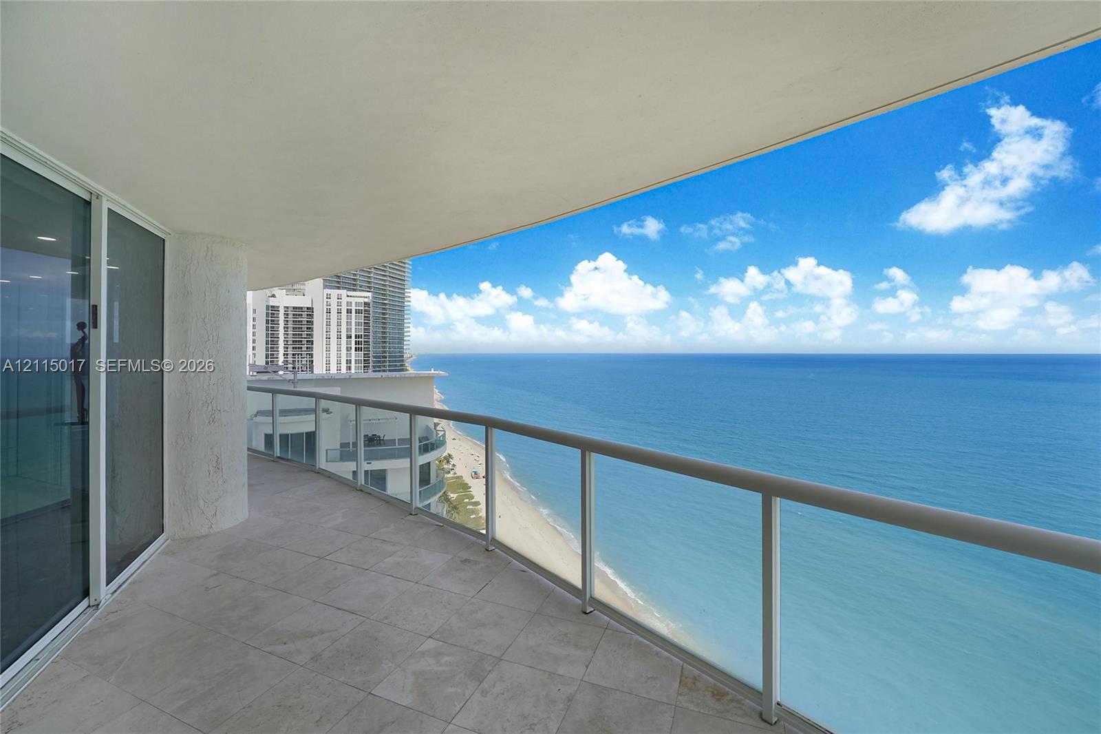 Curved balcony featuring large-format tile flooring, a glass panel railing, and expansive coastal scenery