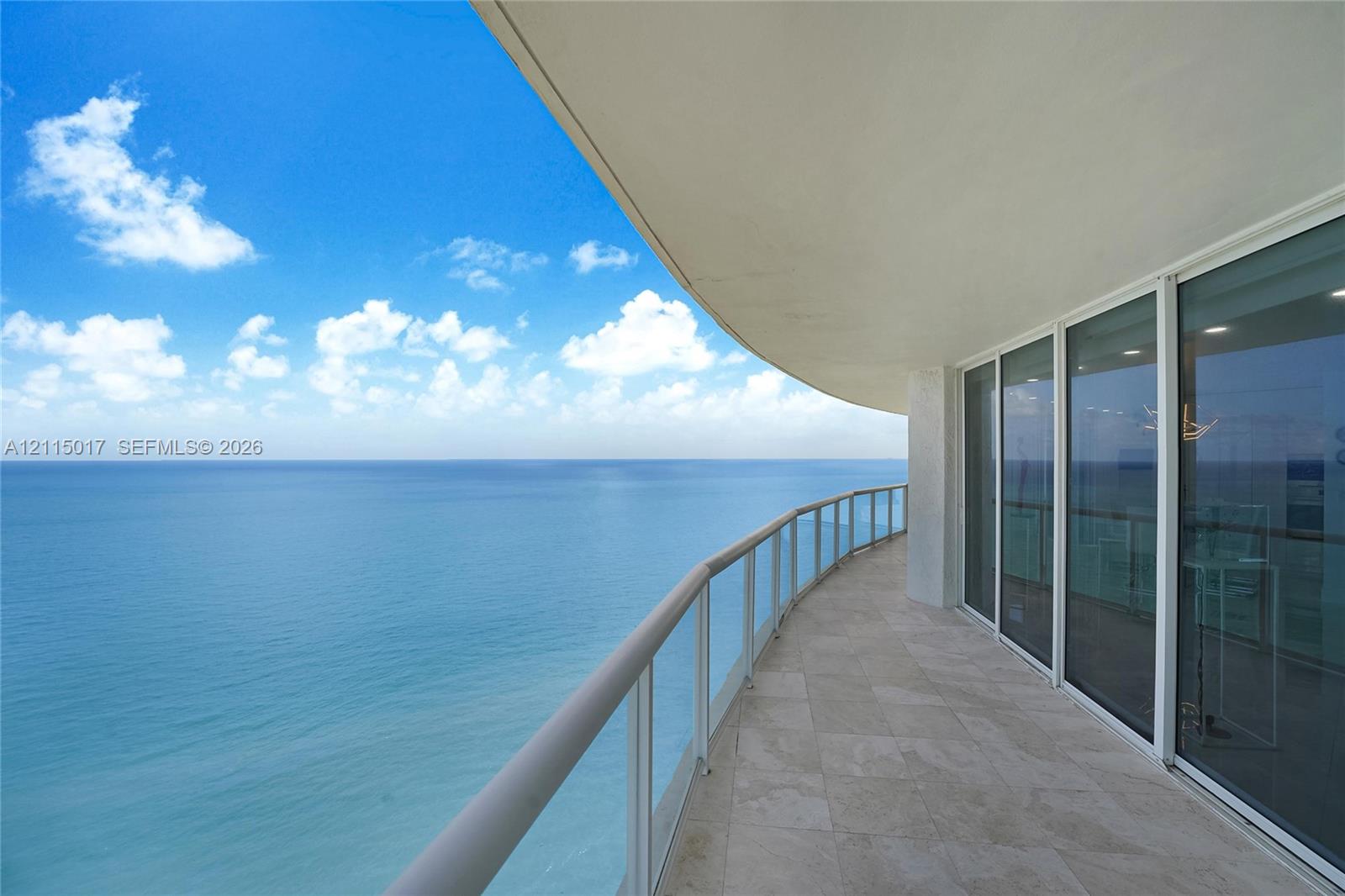Covered balcony featuring natural stone flooring, glass panel railings, and floor-to-ceiling sliding glass doors with ocean exposure