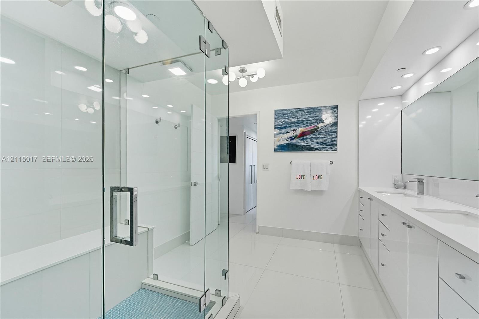 Frameless glass-enclosed shower, dual-sink vanity with high-gloss cabinetry, recessed ceiling lighting, and large-format tile flooring