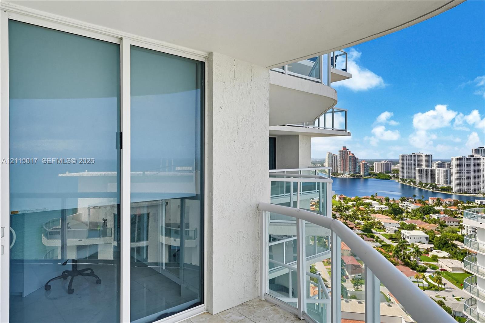 Curved private balcony featuring stone flooring, a glass-panel railing, and oversized floor-to-ceiling sliding glass doors