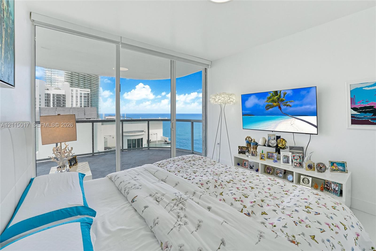 Floor-to-ceiling sliding glass doors opening to a private balcony with glass railing, showcasing expansive ocean scenery