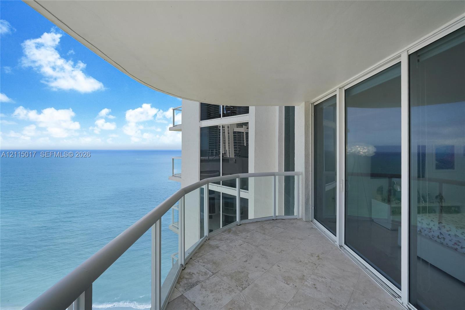 Covered balcony featuring stone flooring and a glass-paneled railing, accessible through floor-to-ceiling sliding glass doors