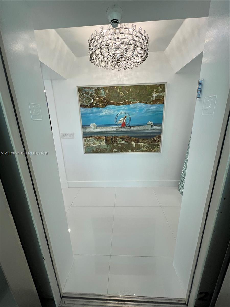 Entryway featuring large-format white tile flooring, a tiered crystal drum chandelier, and a recessed ceiling cove