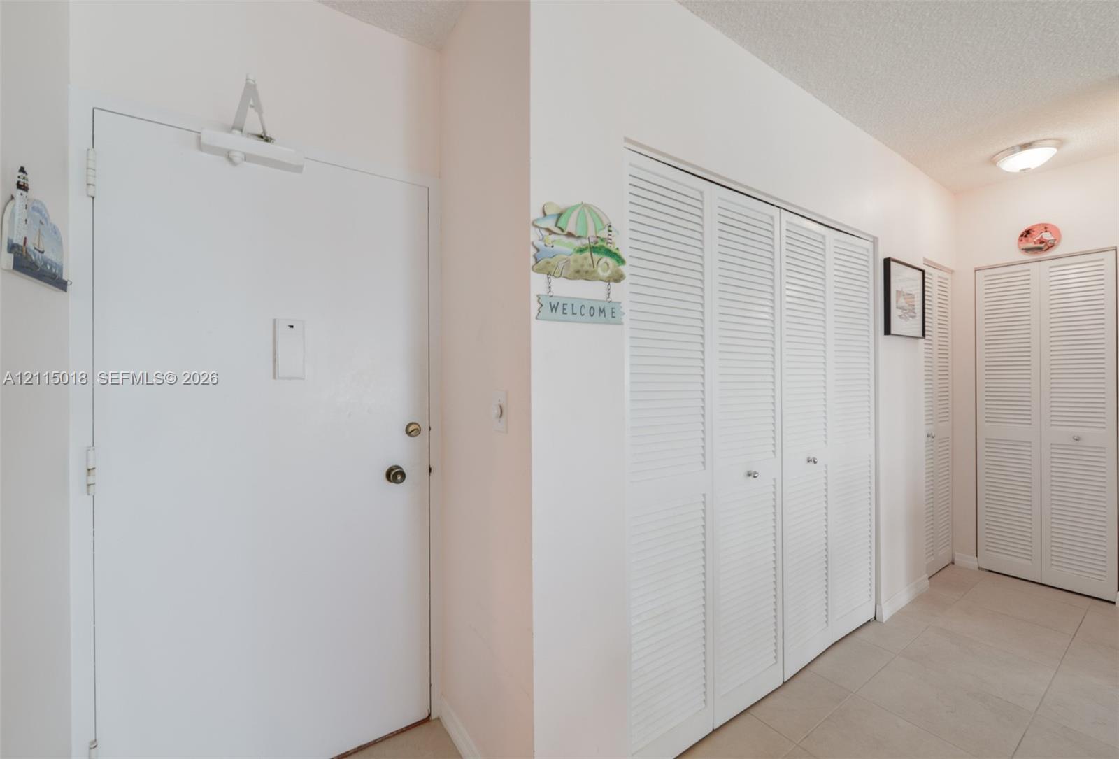 Solid core entry door with overhead hydraulic closer, louvered bi-fold closet doors, and ceramic tile flooring