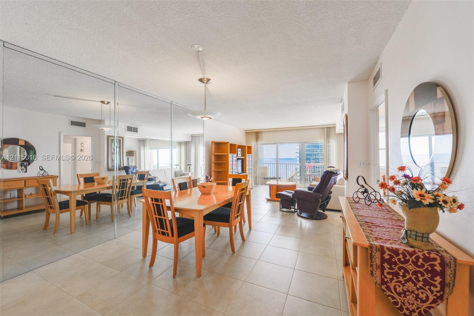 Open-concept interior featuring large-format tile flooring, a floor-to-ceiling mirrored wall, recessed lighting, and a private balcony with glass sliding doors