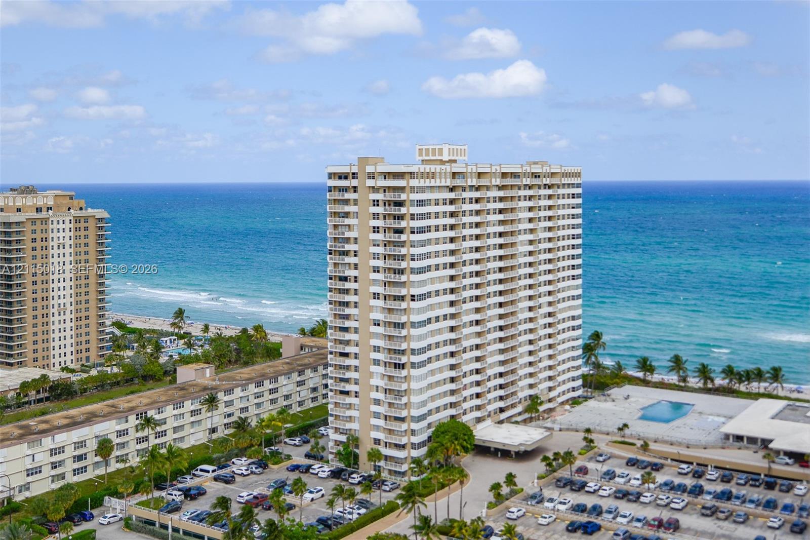 High-rise building featuring private balconies, an outdoor swimming pool, and dedicated surface parking, positioned along the coastline