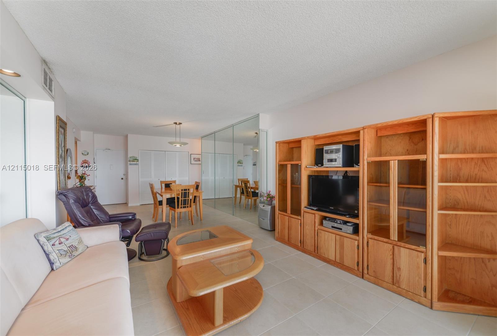Large built-in light-tone wood shelving unit with glass-paneled cabinetry, mirrored wall panels, and tile flooring