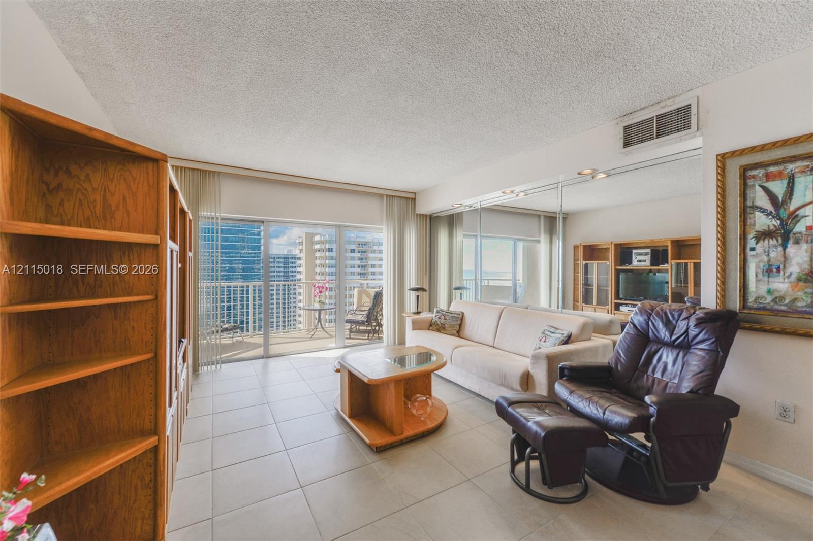 Large-format tile flooring, mirrored wall accents, built-in wooden shelving, and floor-to-ceiling glass doors opening to a balcony