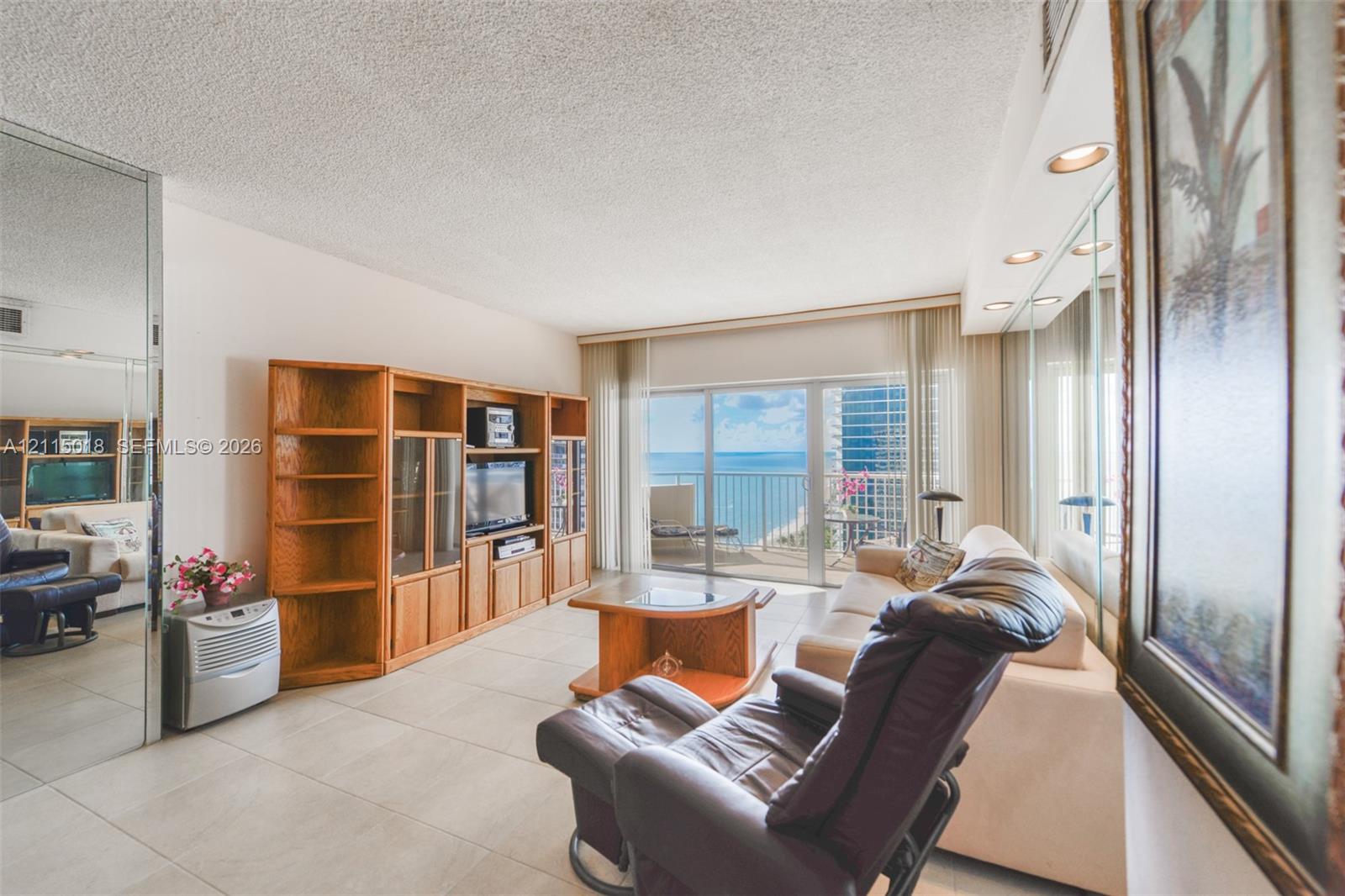 Large-format tile flooring, built-in wooden cabinetry, recessed ceiling lighting, wall-to-wall mirrored paneling, and sliding glass doors opening to a balcony