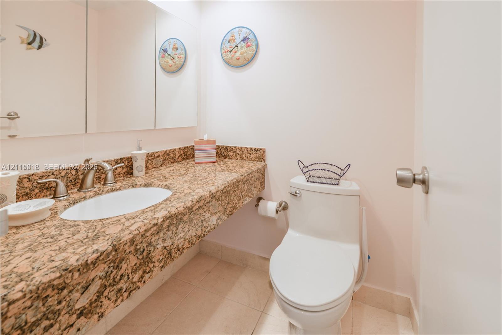 Neutral stone countertop with an integrated oval sink, brushed nickel faucet, wall-spanning triple-panel mirror, and tile flooring