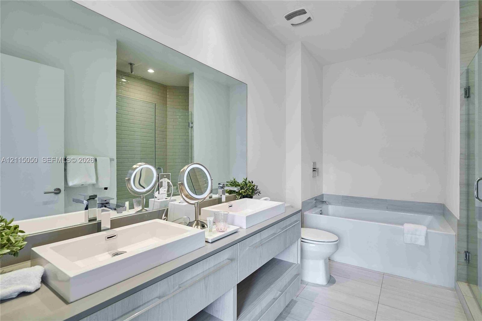 Bathroom featuring a dual-sink floating vanity with rectangular vessel sinks, expansive wall-to-wall mirror, built-in soaking tub, and tiled flooring