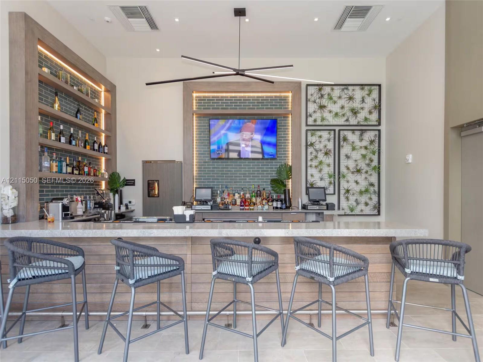 Built-in bar featuring a stone-composite countertop, wood-paneled base, integrated shelving with recessed lighting, and a linear modern pendant light fixture