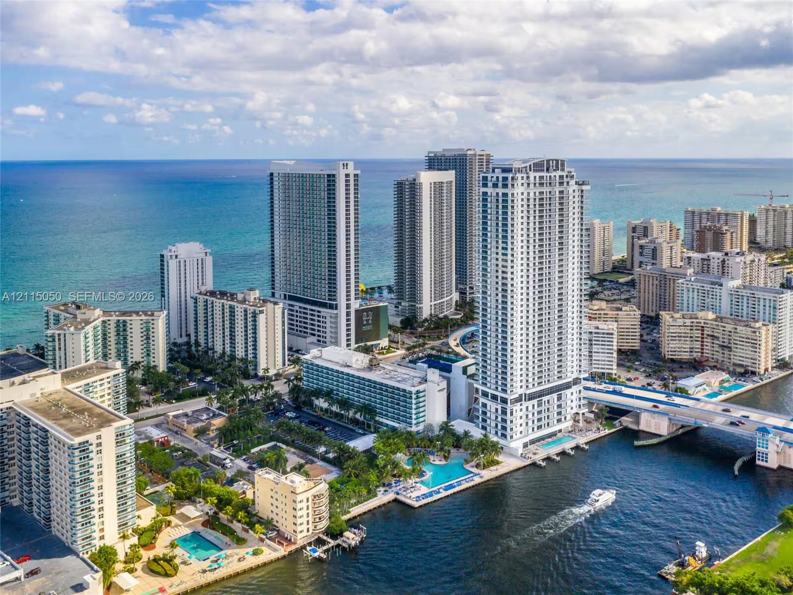 Aerial perspective of a high-rise urban environment featuring coastal proximity, deep-water canal access, bridge infrastructure, and multiple swimming pools