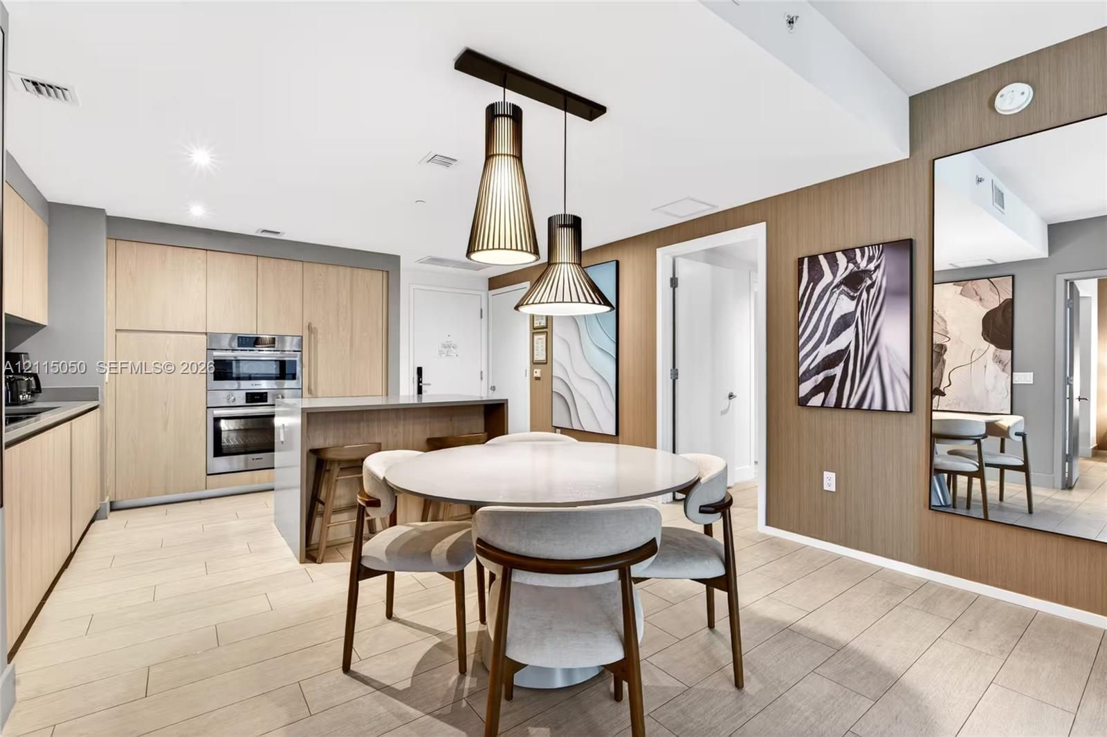 Kitchen featuring flat-panel wood-finish cabinetry, built-in stainless steel double wall ovens, a central island, modern pendant lighting, and wood-finish flooring Kitchen featuring flat-panel wood-finish cabinetry, built-in stainless steel double wall ovens, a central island, modern pendant lighting, and wood-finish flooring