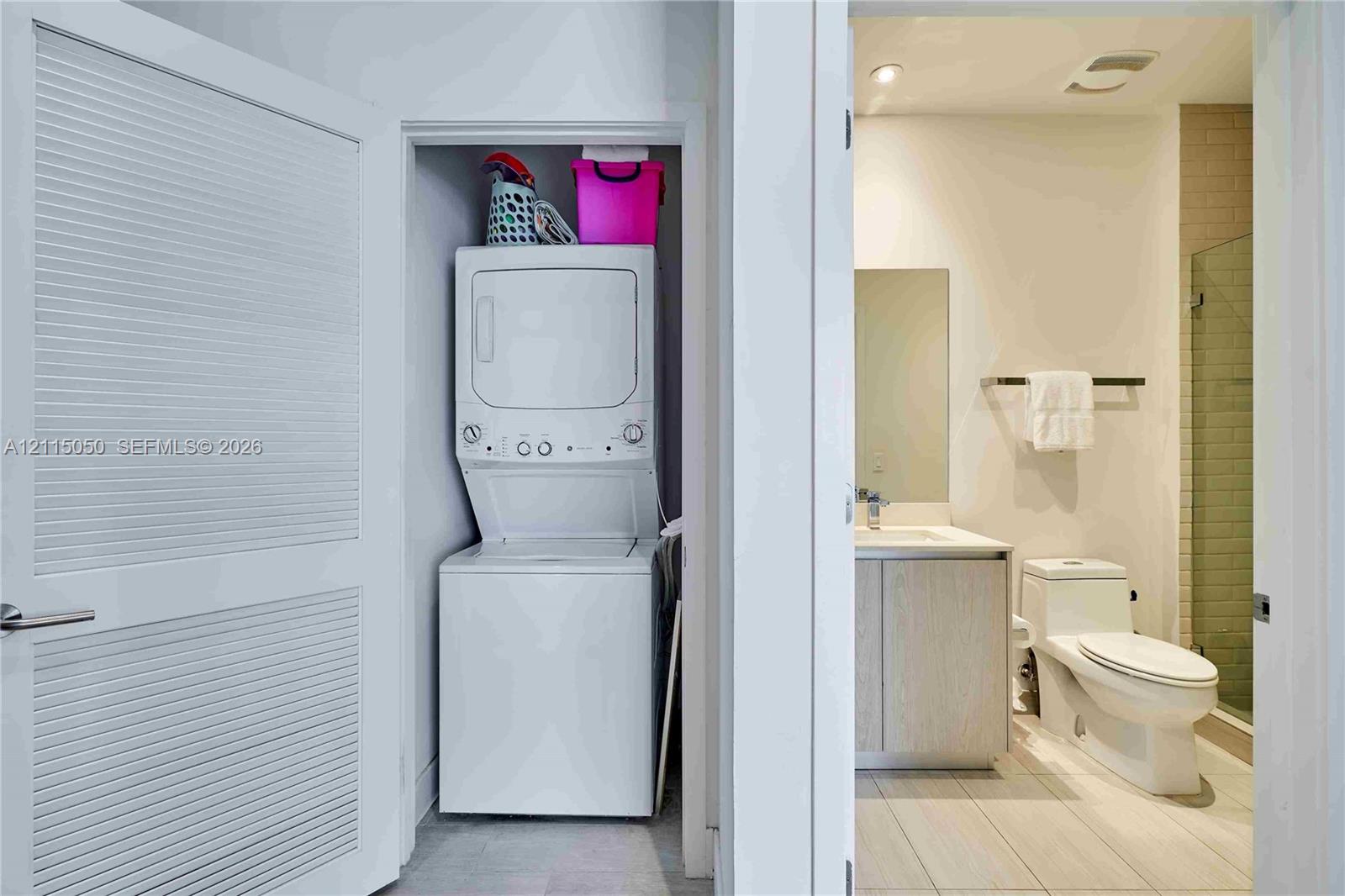 Laundry closet featuring a stacked washer and dryer, paired with a bathroom containing a vanity, a toilet, and a glass-enclosed shower with tiled walls