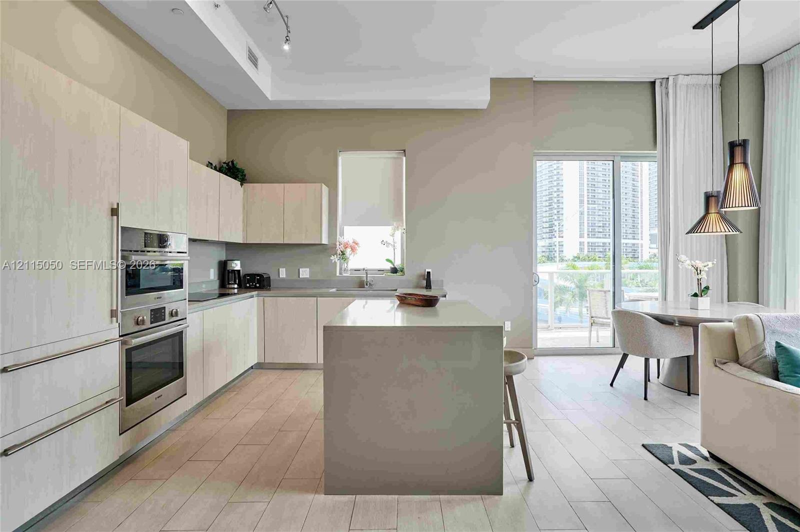 Kitchen featuring light wood-finish cabinetry, a central island with a solid surface countertop, stainless steel double wall ovens, wood-finish flooring, and dual pendant lighting Kitchen featuring light wood-finish cabinetry, a central island with a solid surface countertop, stainless steel double wall ovens, wood-finish flooring, and dual pendant lighting